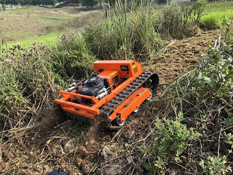 An orange, tracked electric lawnmower is cutting grass across rugged terrain.